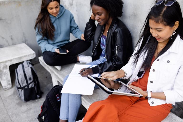 group of students look at their phones, tablets and notebook together