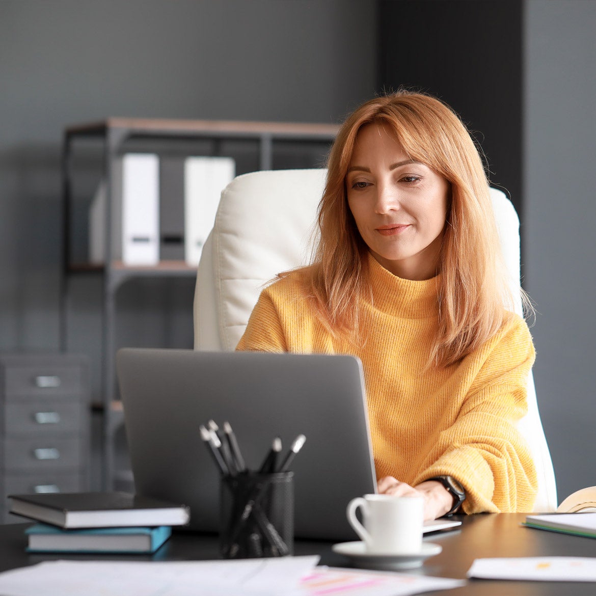 Woman in yellow sweater sitting at desk using a laptop