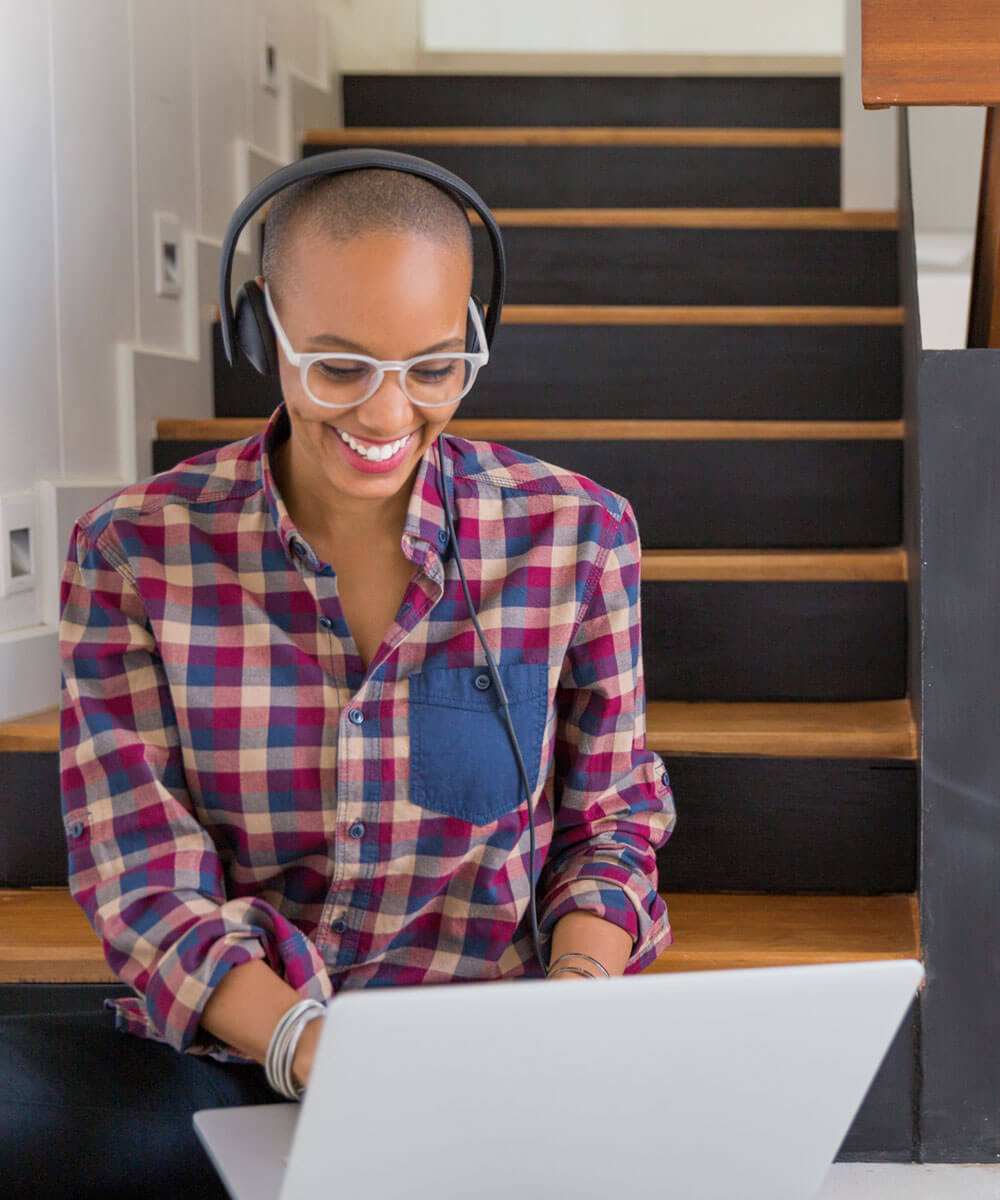 person sitting on stairs working on laptop with headphones on